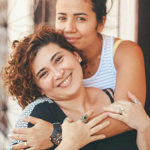 Latina woman in white tank top hugging older woman in blue tank top