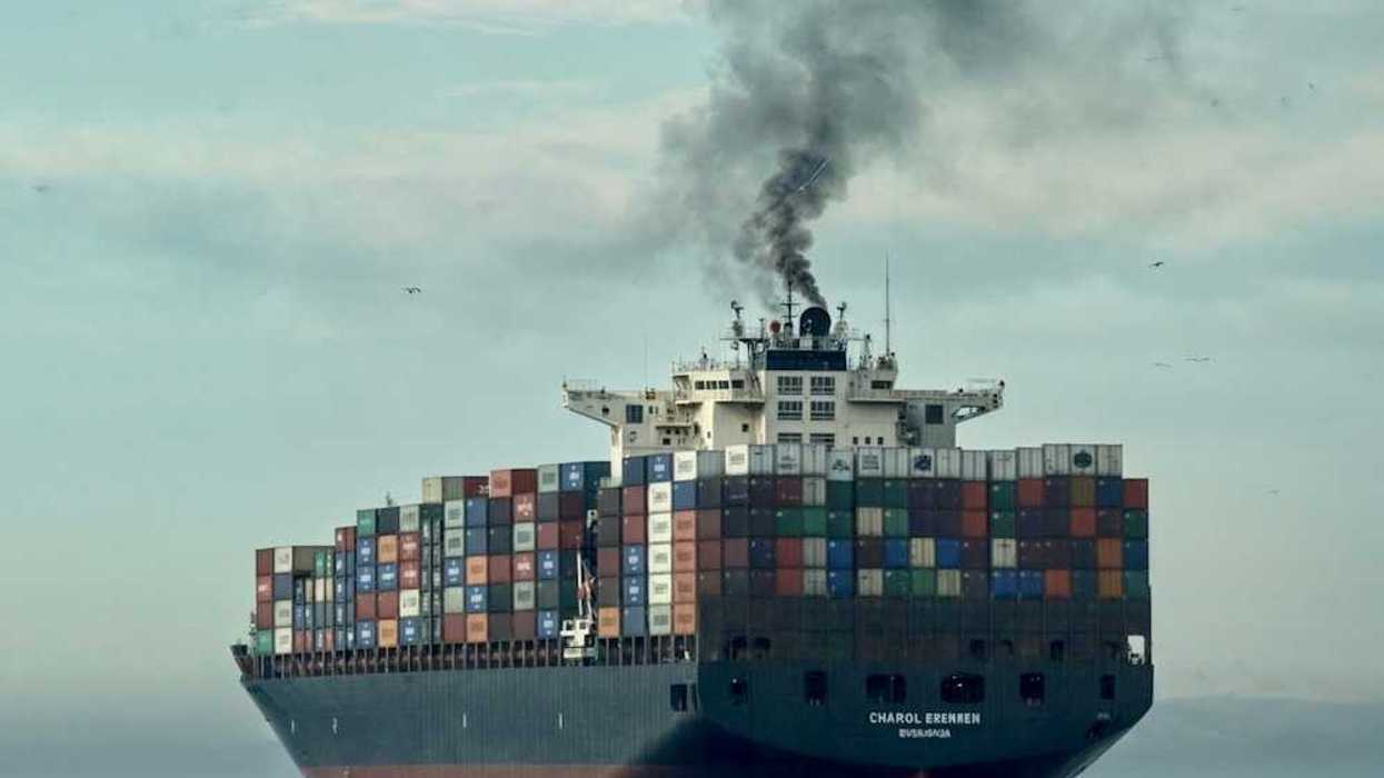 Loaded container ship on open sea belching black smoke
