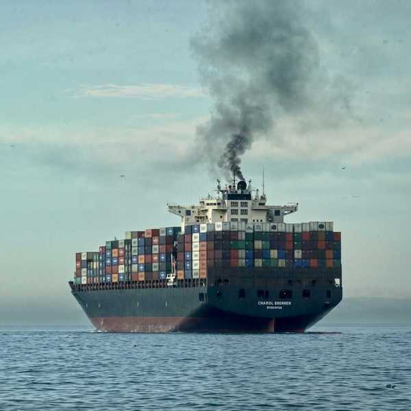 Loaded container ship on open sea belching black smoke