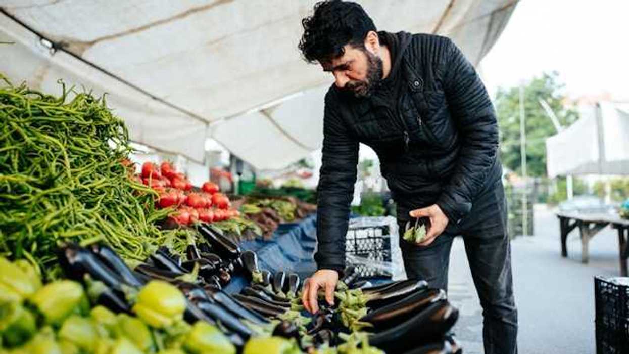 Man at an outdoor farmer's market looking at eggplant
