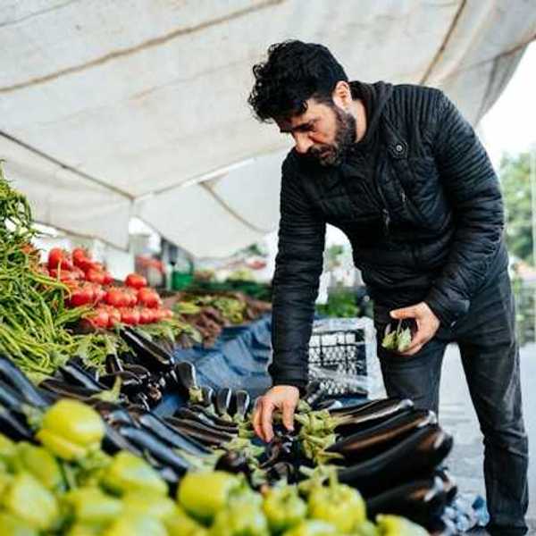 Man at an outdoor farmer's market looking at eggplant