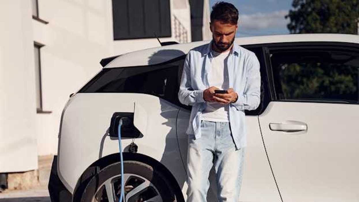Man checking his phone while waiting for his electric vehicle to charge