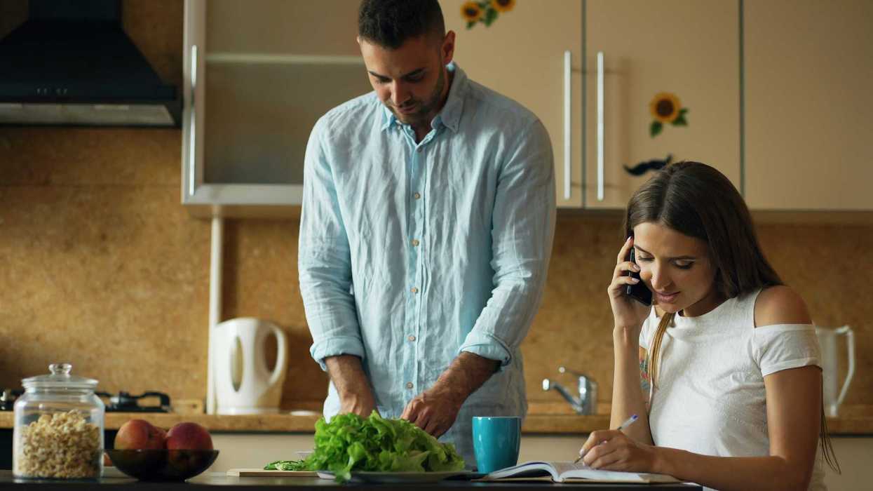 Man chopping vegetables while woman talks on phone.