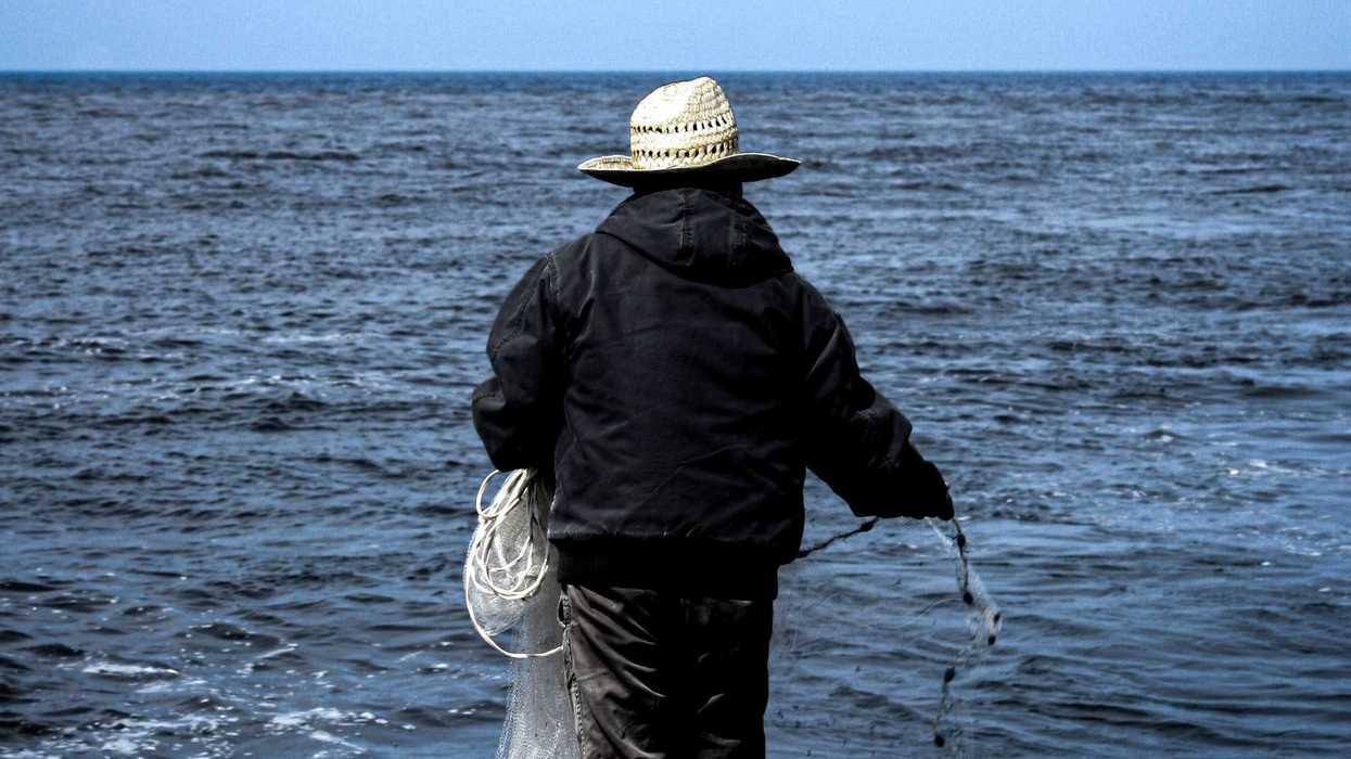 man fishing in black jacket and brown hat holding stick near body of water during daytime.