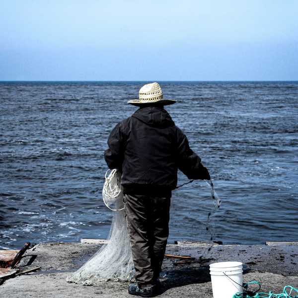 man fishing in black jacket and brown hat holding stick near body of water during daytime.