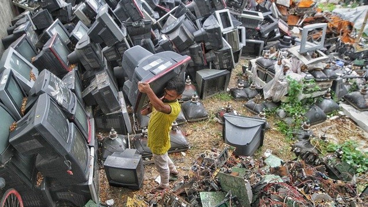 man holding a TV near dozens of other discarded TVs