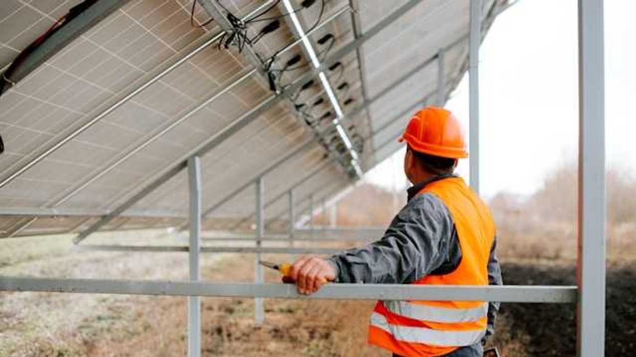 Man in an orange safety vest standing under a solar panel