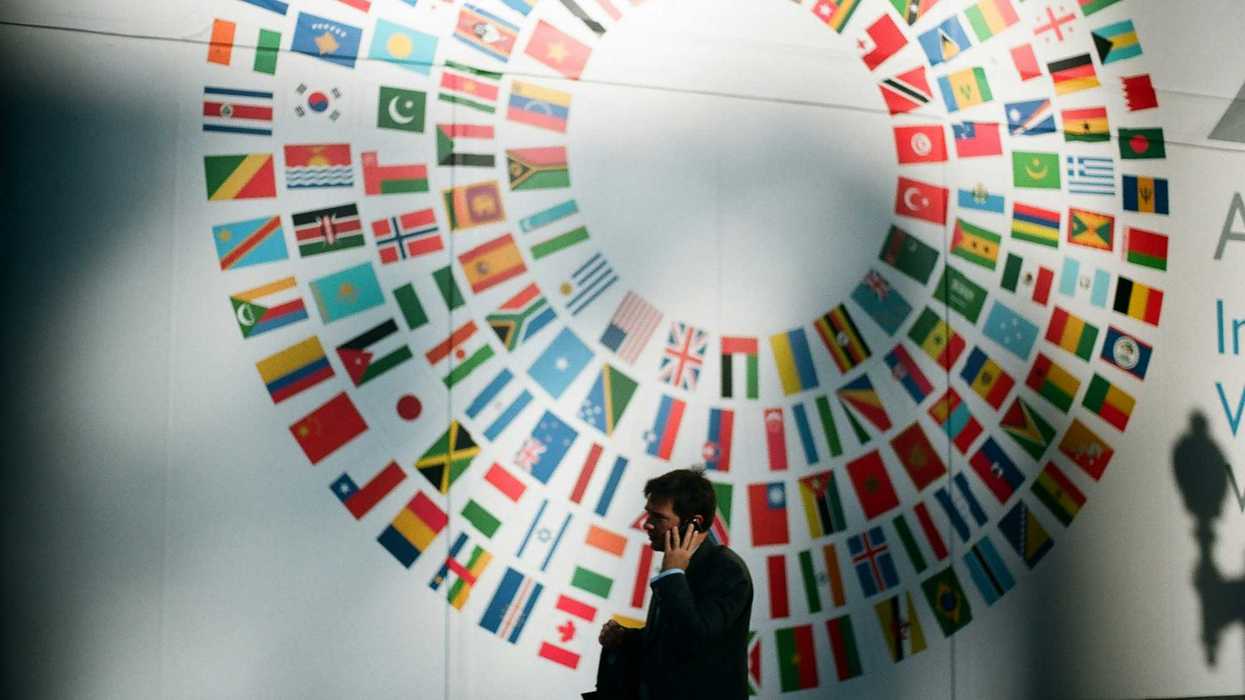 man in black coat standing near round white red and blue wall with a circle of flags of the world on it.