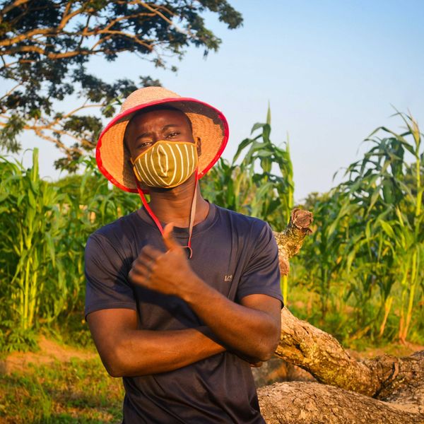 man in brown crew neck t-shirt wearing brown hat standing in front of a row of crops