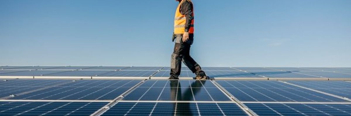 Man in safety vest and hard hat walking between solar panels.
