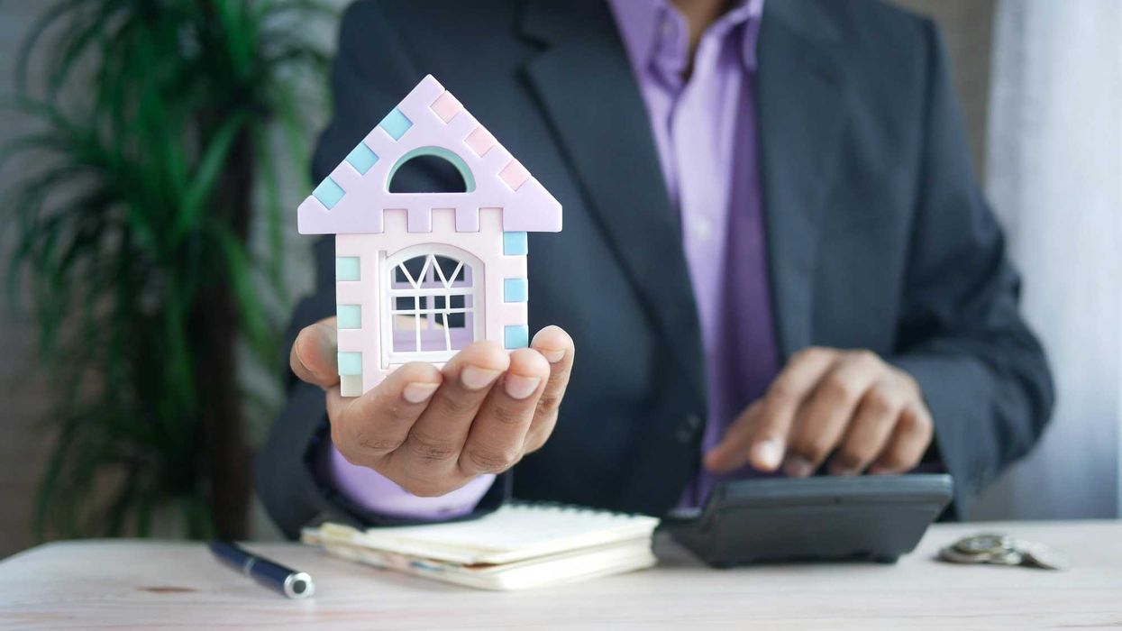 man in suit holding a toy model of a house and using a calculator