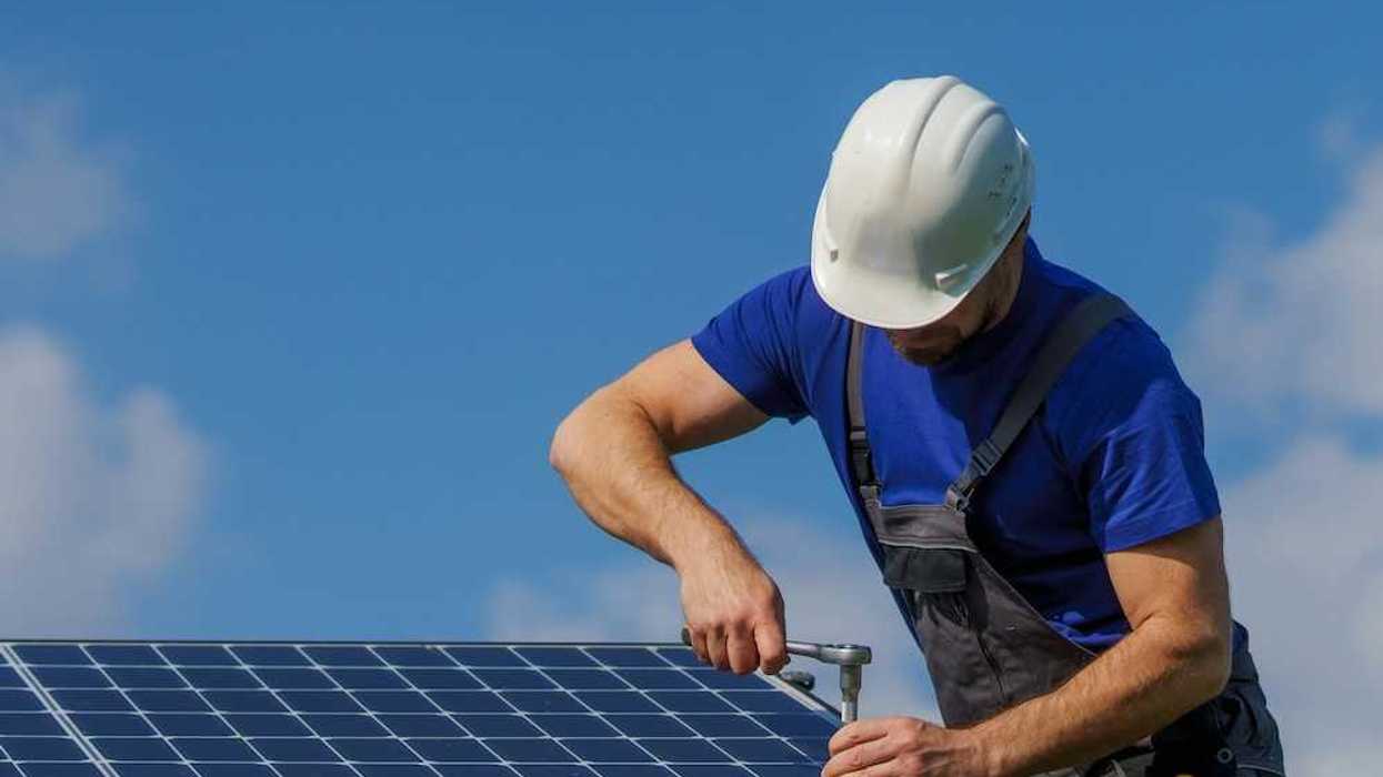 Man in white hard hat and blue shirt installing solar panels