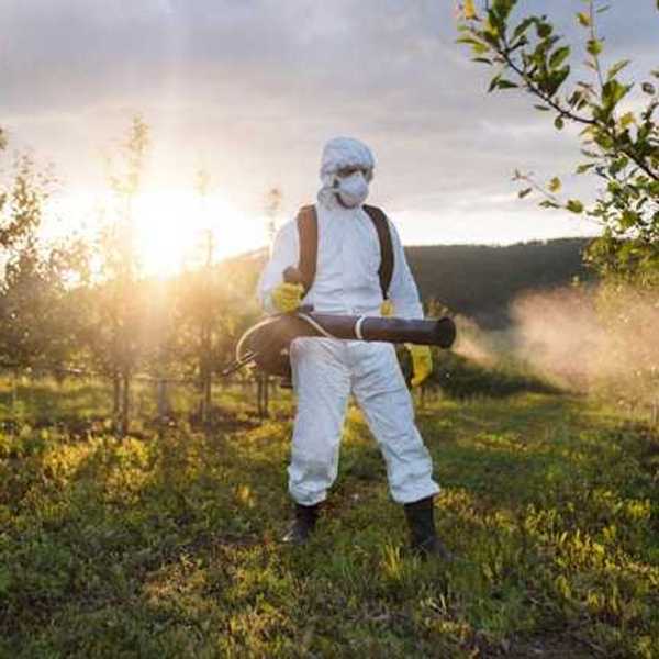 Man in white hazmat suit spraying herbicide in a field