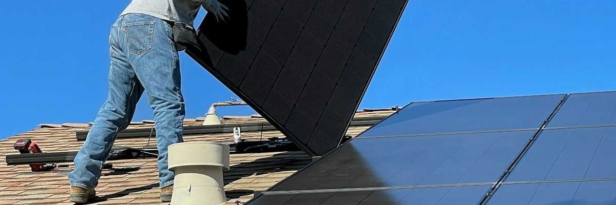 Man installing solar panels on house roof.