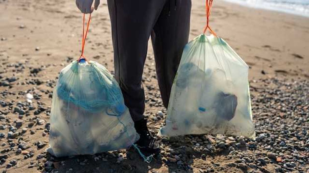 Man on a beach holding two large plastic bags filled with plastic trash
