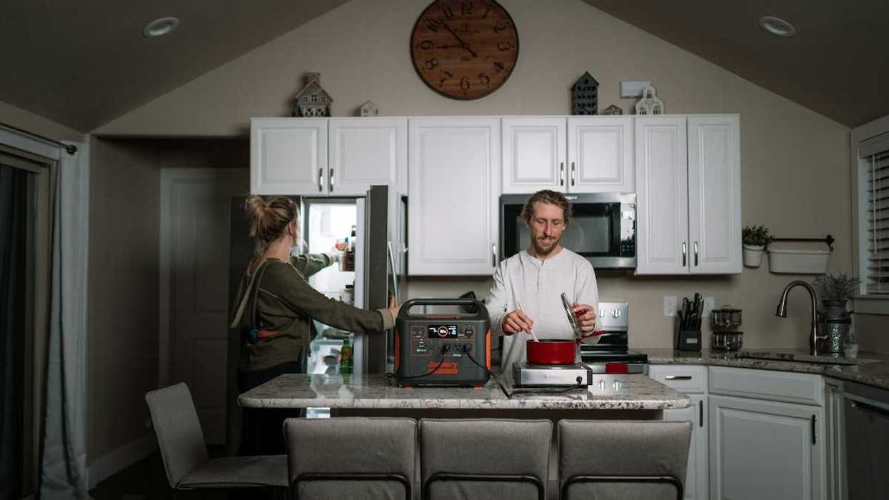 Man prepares dinner in kitchen while woman opens refrigerator during power outage while appliances are powered by a portable power station.