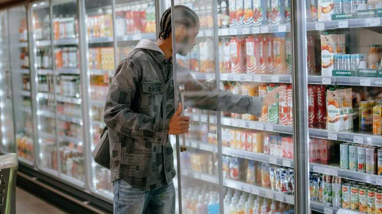 Man reaching into a supermarket refrigeration cooler for a carton of milk