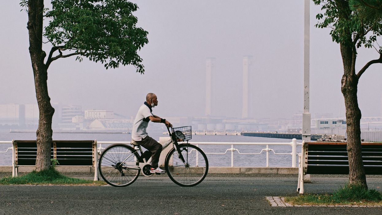 Man riding a bicycle along a waterfront path with hazy air and a river in background.
