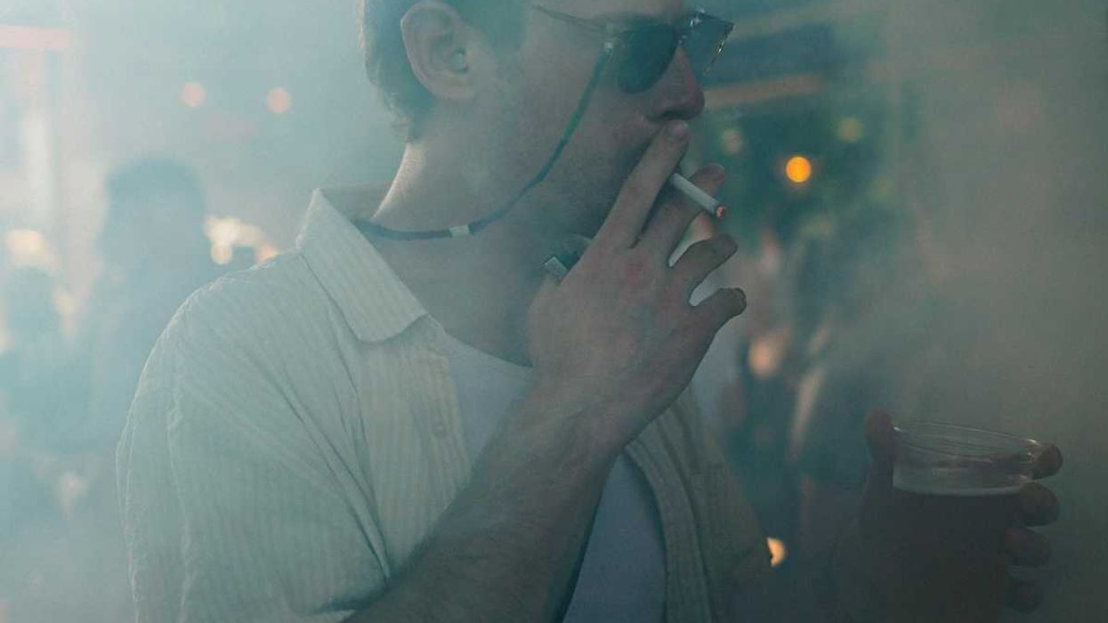 Man smoking cigarette and holding beer in smoky room