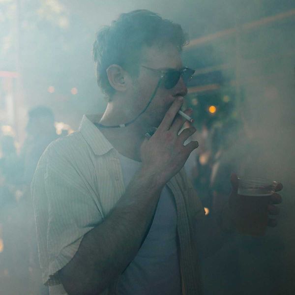 Man smoking cigarette and holding beer in smoky room