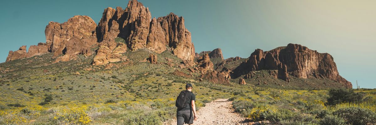 man walking up towards hill in dry, rocky desert environment.