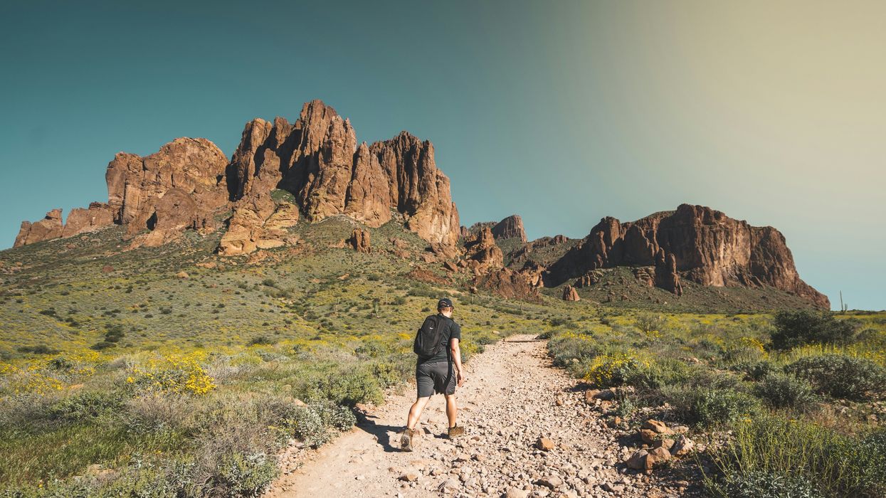 man walking up towards hill in dry, rocky desert environment.