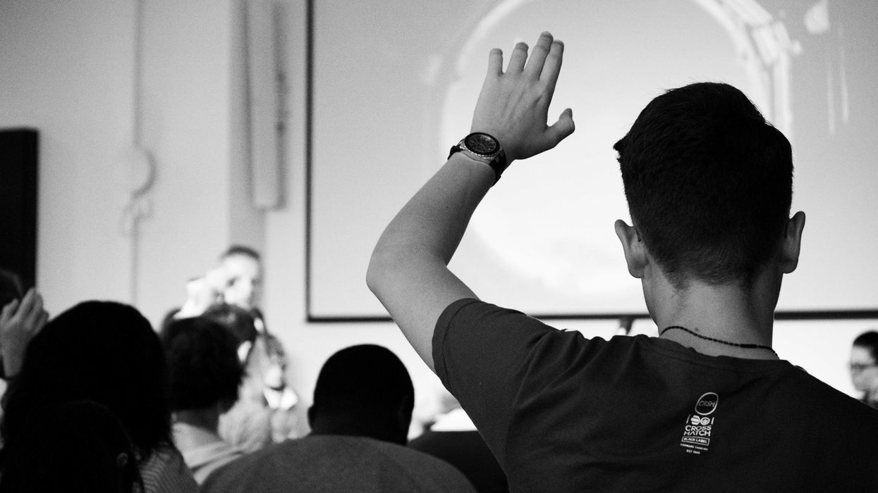 man wearing black t-shirt close-up photography raising his hand in a college classroom