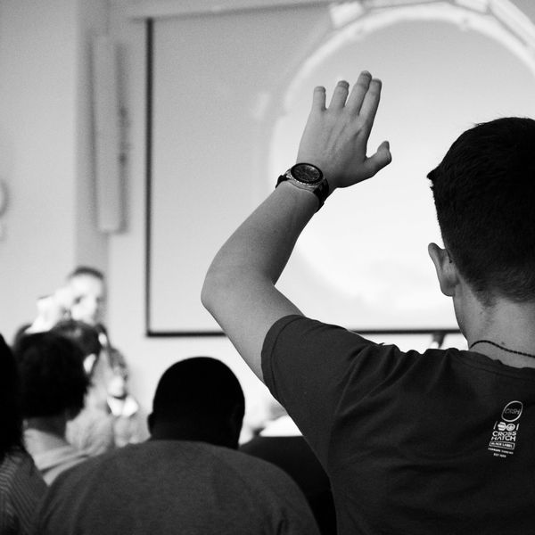 man wearing black t-shirt close-up photography raising his hand in a college classroom