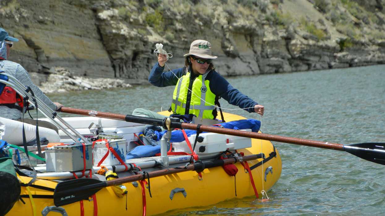 man wearing green safety vest riding yellow inflatable boat on a river.