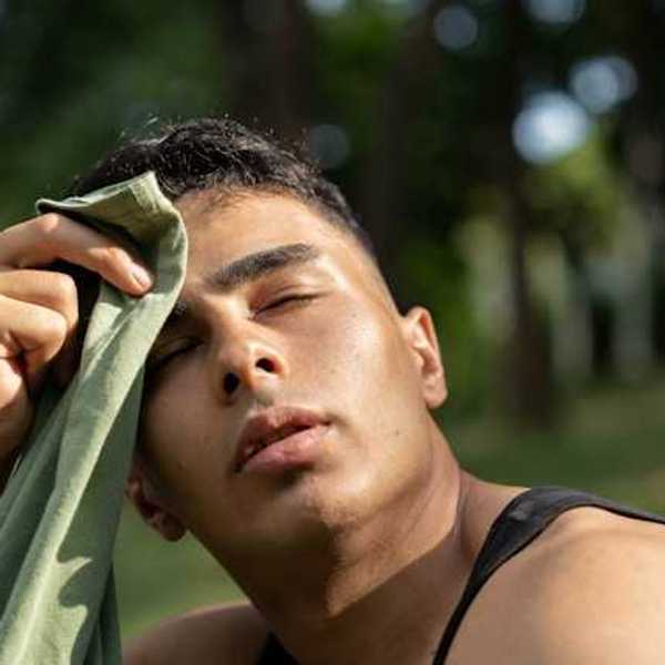 Man wiping the sweat off of his forehead with a shirt while sitting outside in a park