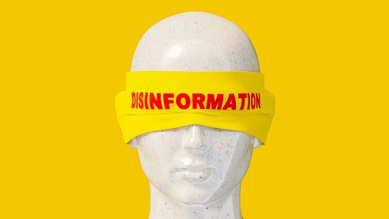Mannequin head shot wearing a yellow blindfold labeled "disinformation" in red letters.