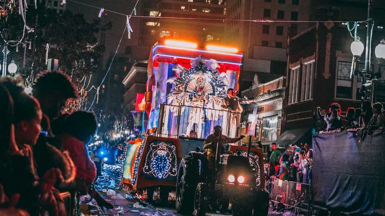 Mardi Gras parade after dark - tractor pulling float through spectator-lined street amidst accumulated trash