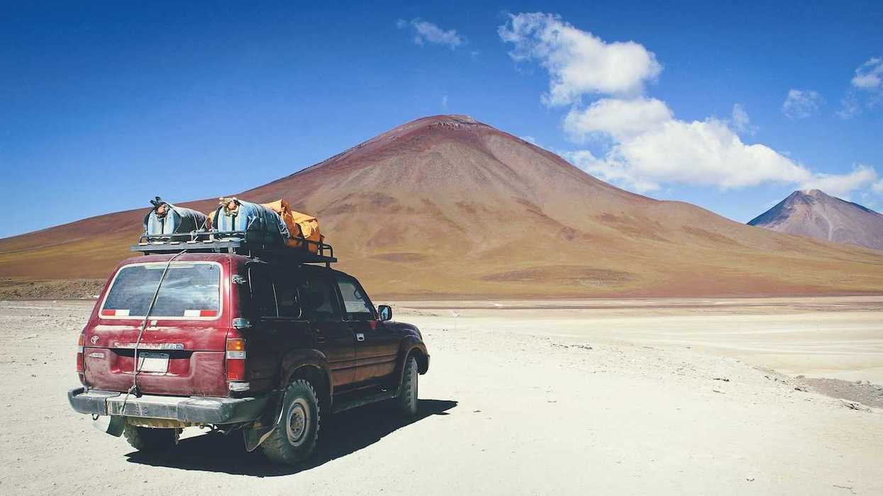Maroon SUV with baggage on roof rack facing mountains in Bolivian outback