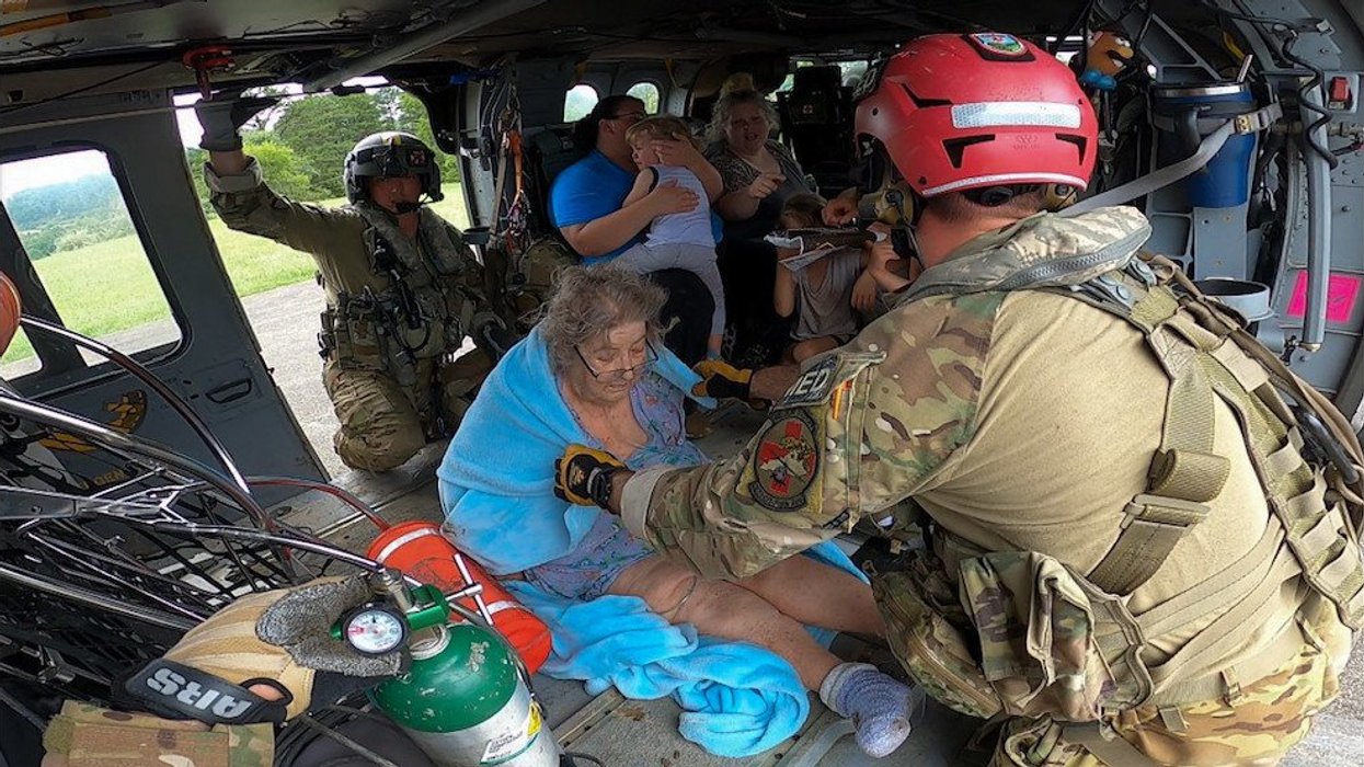 Members of the National Guard assist an elderly woman and other survivors of an extreme weather event.