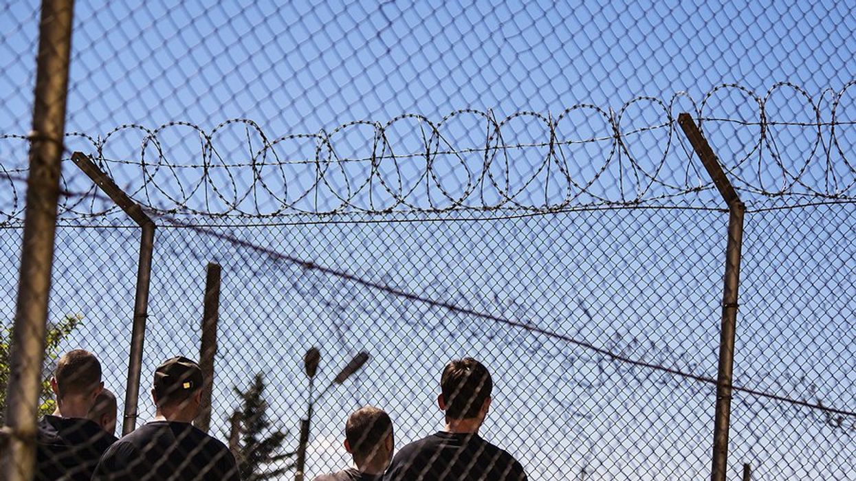 Men standing behind barbed wire fences.