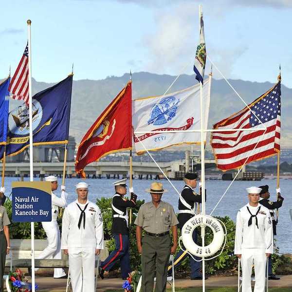 Military and NPS personnel at Pearl Harbor ceremony, standing at attention with color guard carrying flags behind