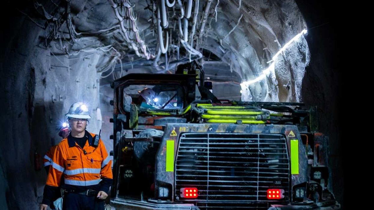 Miner in reflective orange jacket working underground alongside boring machine