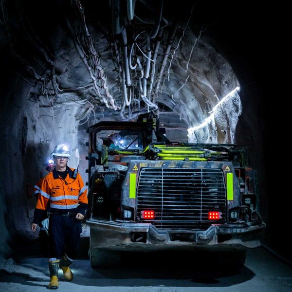 Miner in reflective orange jacket working underground alongside boring machine