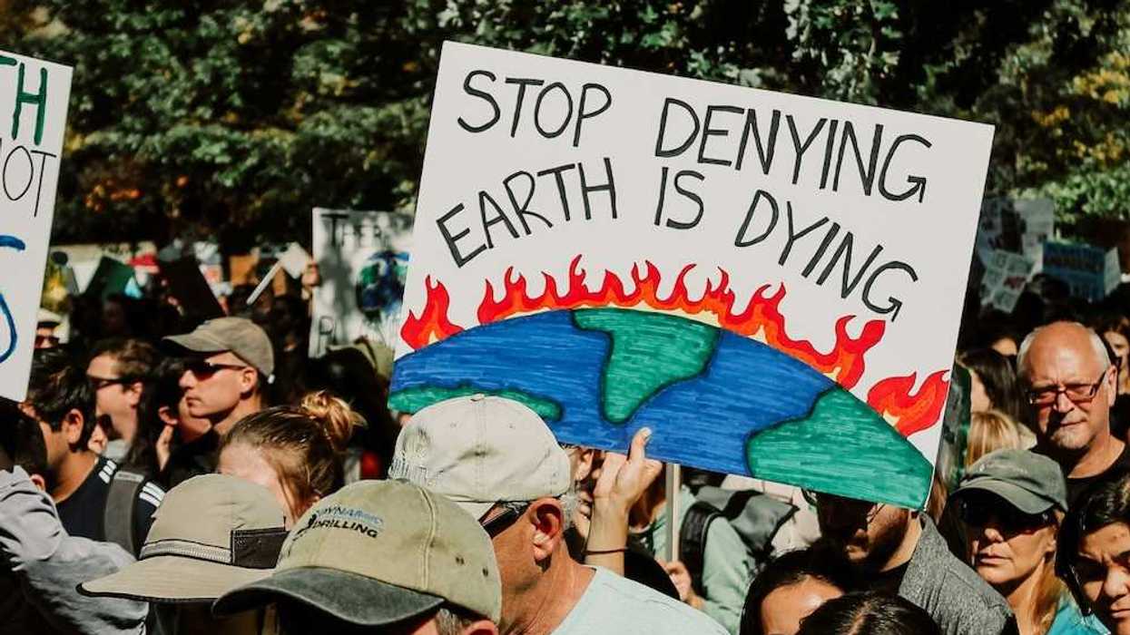Mixed crowd taking part in climate protest prominently featuring a sign reading, "Stop Denying Earth is Dying"
