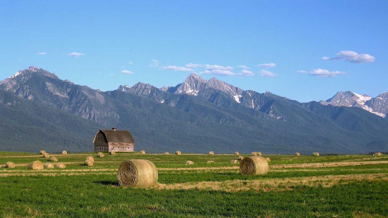 Montana landscape with barn and round-baled hay against snow-capped Rocky Mountains