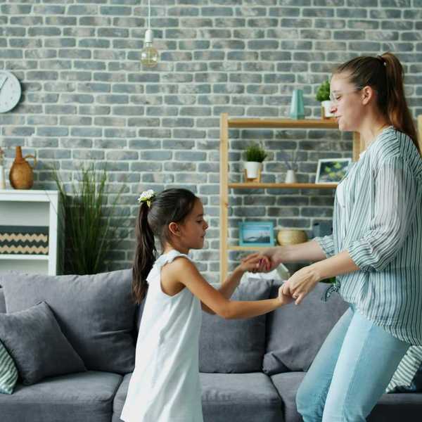 Mother and daughter dancing together in living room.