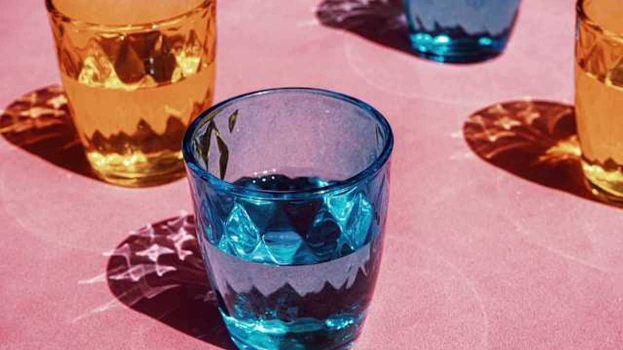 Multicolored drinking glasses filled with water on a pink surface