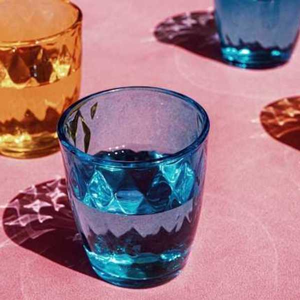 Multicolored drinking glasses filled with water on a pink surface