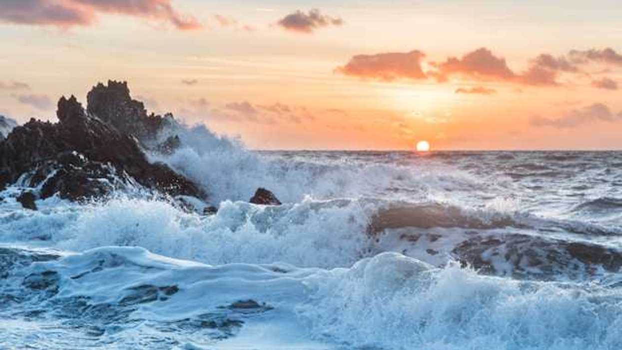 Ocean waves breaking on a beach with the sun setting in the background