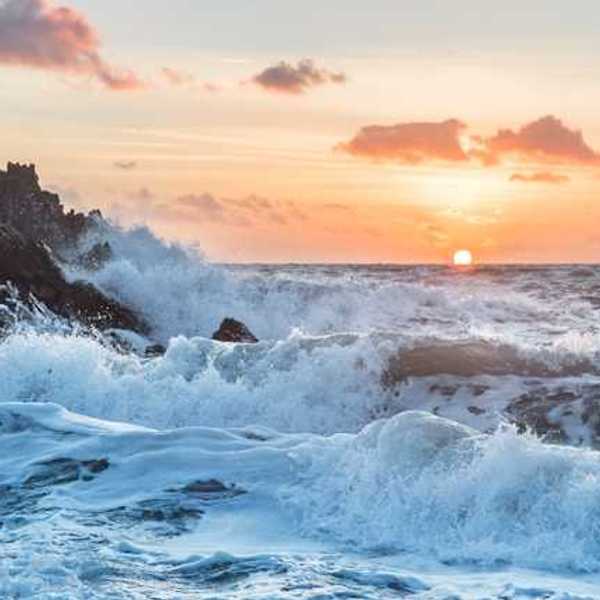 Ocean waves breaking on a beach with the sun setting in the background