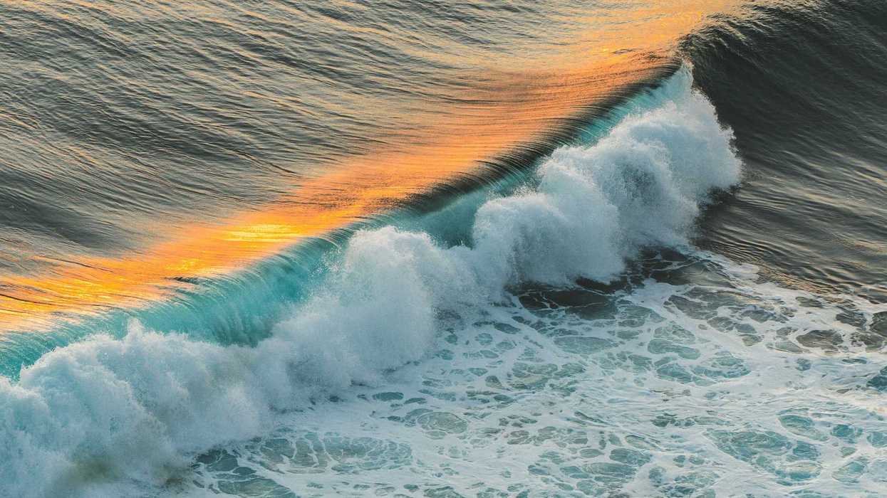 ocean waves crashing on shore during daytime with a strip of orange sunset light reflecting on surface.