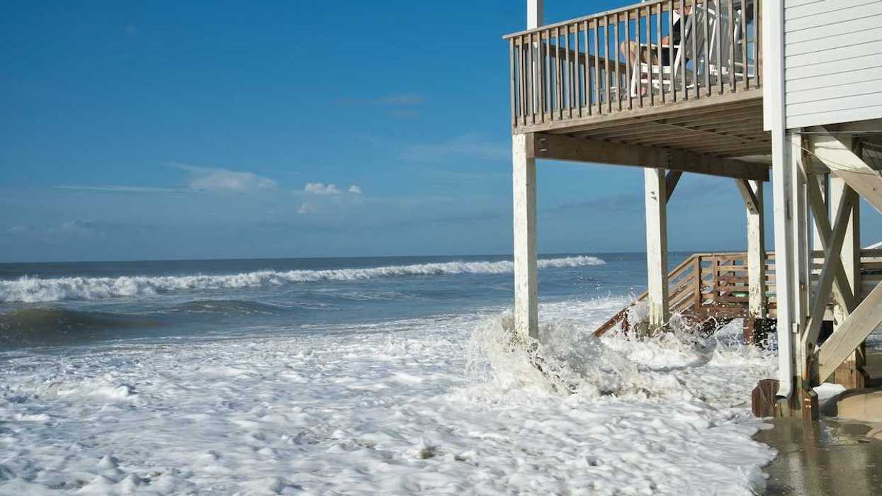 Ocean waves lap against the piers supporting a seaside home