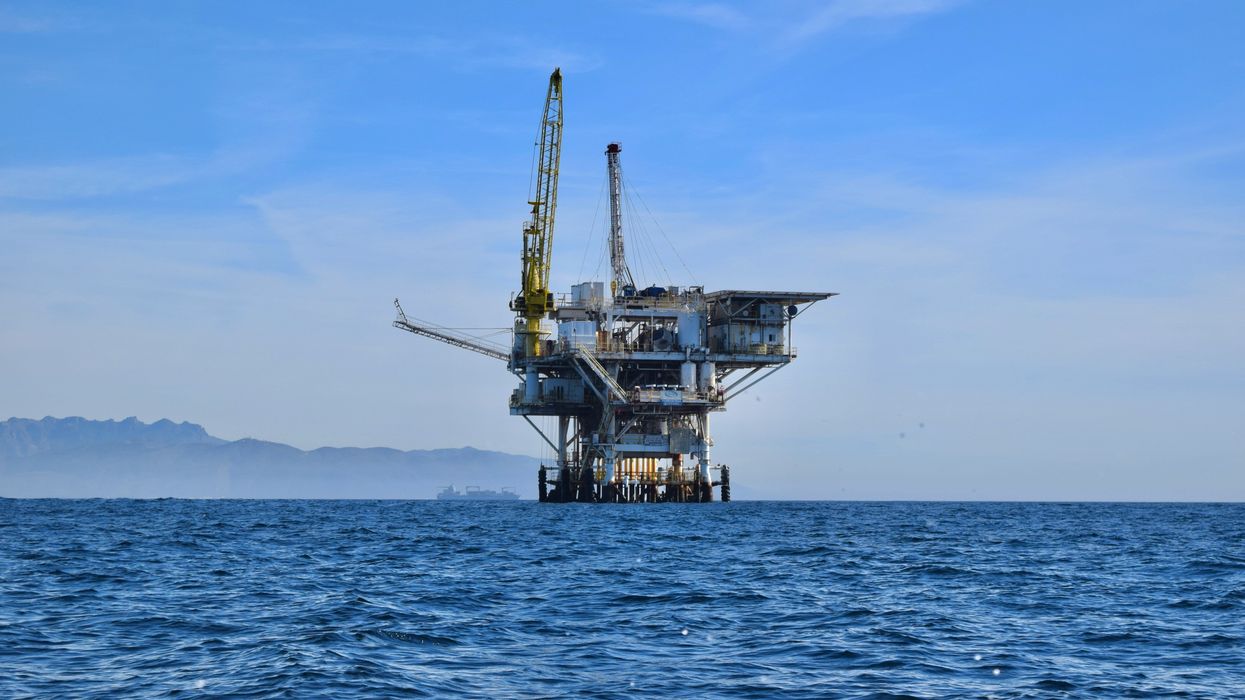 Offshore oil rig with mountainous coastline in background.