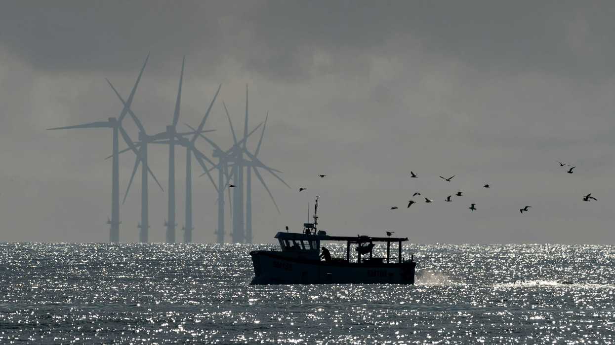 Offshore wind turbines with a fishing boat and birds flying in the foreground.
