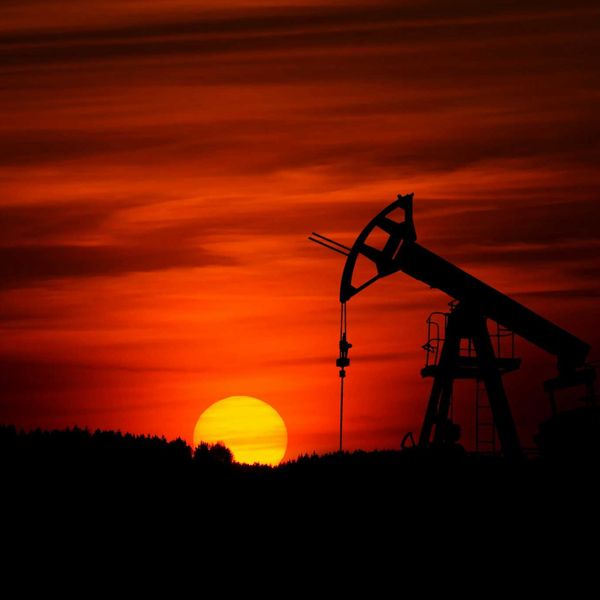 Oil drilling rig silhouetted against a red sunset sky.